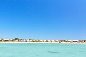 A beachfront hotel with multiple buildings, a sandy beach, and clear blue skies.