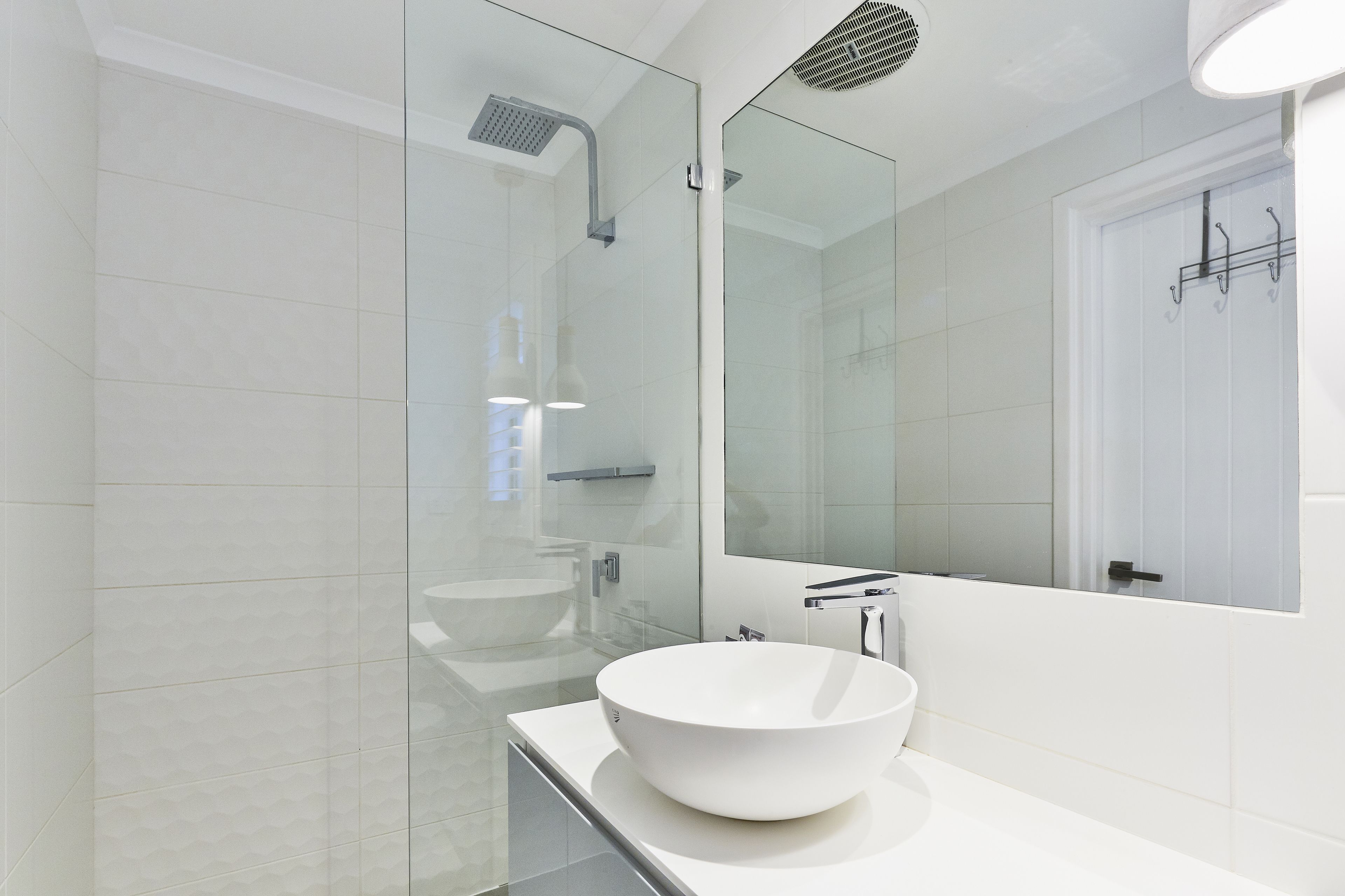 Une salle de bain moderne avec une douche à parois de verre, un lavabo blanc et un grand miroir.