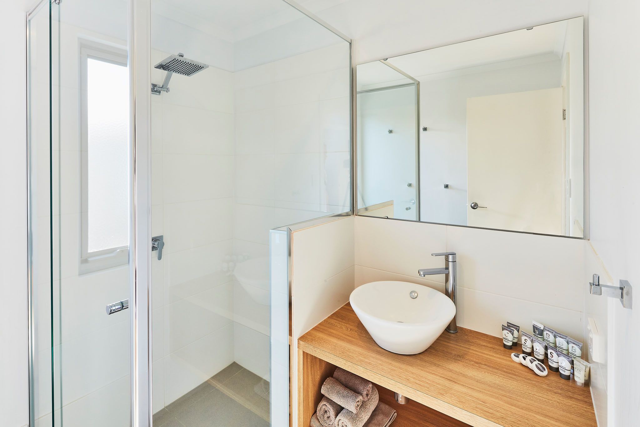A modern bathroom with a glass shower enclosure, a wooden vanity with a white sink, and a large mirror.