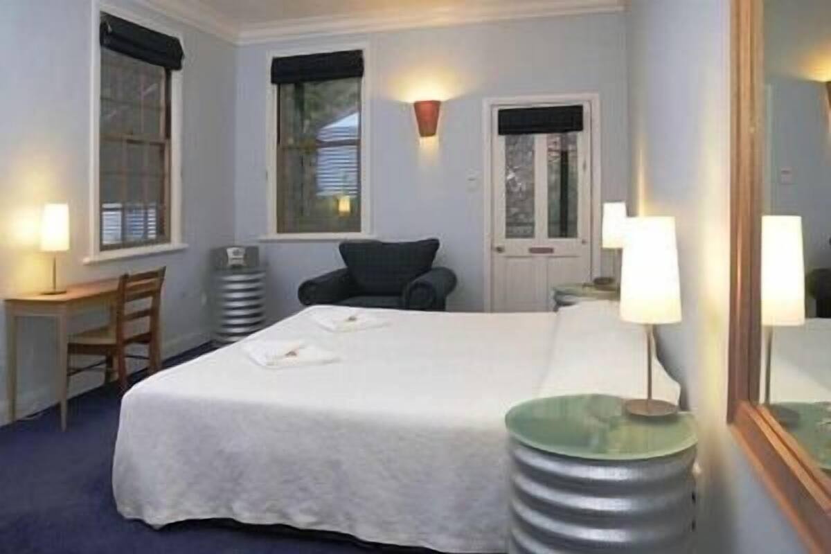 A hotel room with a bed, a desk, a chair, and two windows.