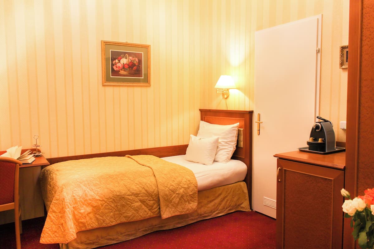 A hotel room with a bed, a nightstand, a lamp, a coffee maker, and a framed picture on the wall.