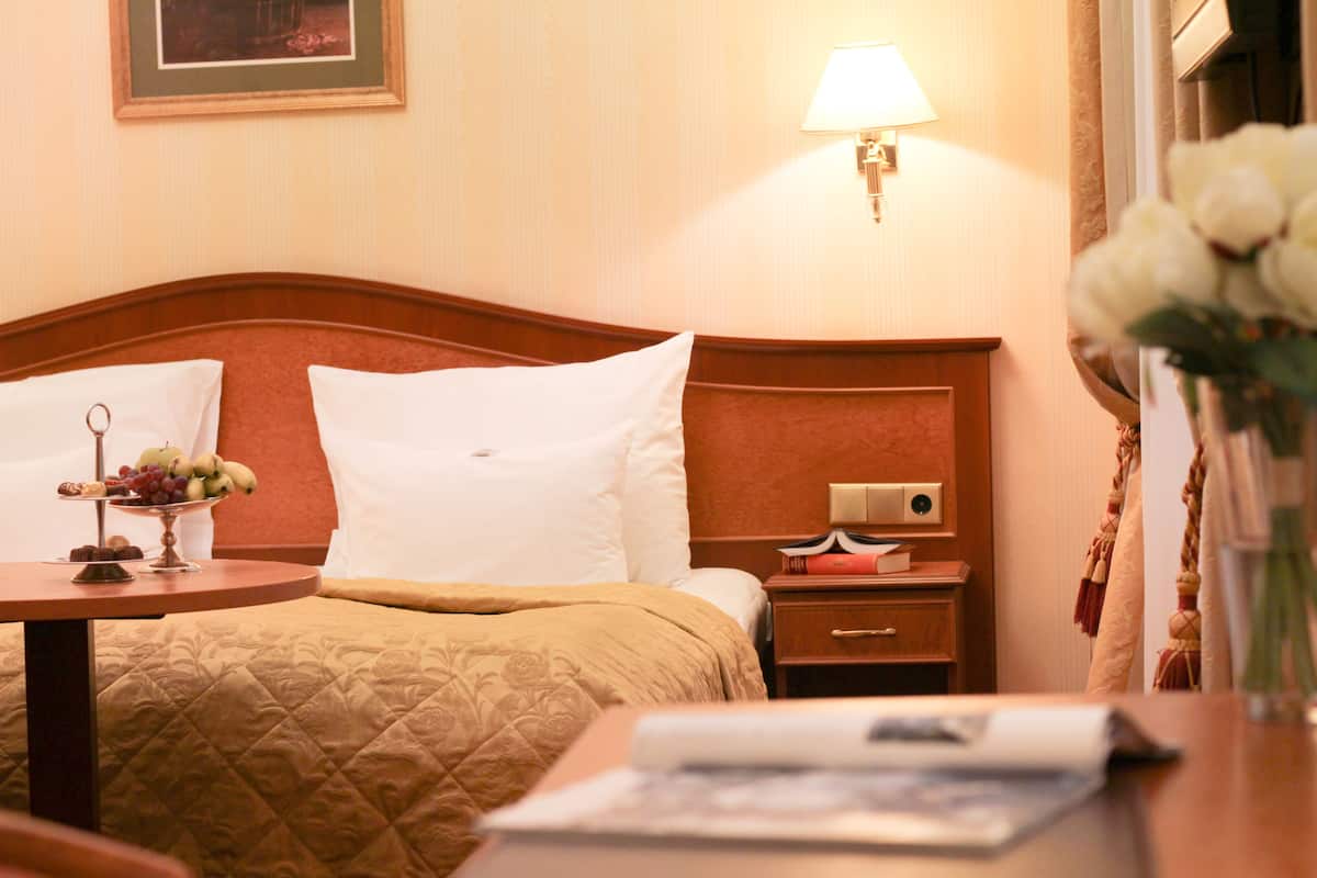 A hotel room with a bed, bedside table, lamp, and a vase with flowers.