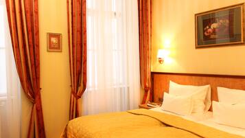 Una habitación de hotel con cama, cortinas, una mesita de noche y una lámpara de pared.