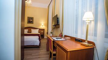 A hotel room with a bed, a desk with a lamp, a TV, and a window with curtains.