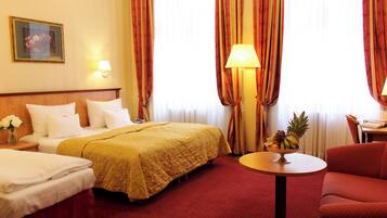 A hotel room with two beds, a red carpet, a round table with fruit, and a lamp.
