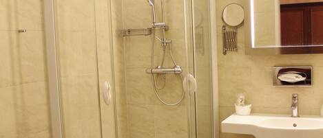 Ducha envuelta en vidrio con cabezal de ducha manual, lavamanos fijado a la pared y espejo sobre él.