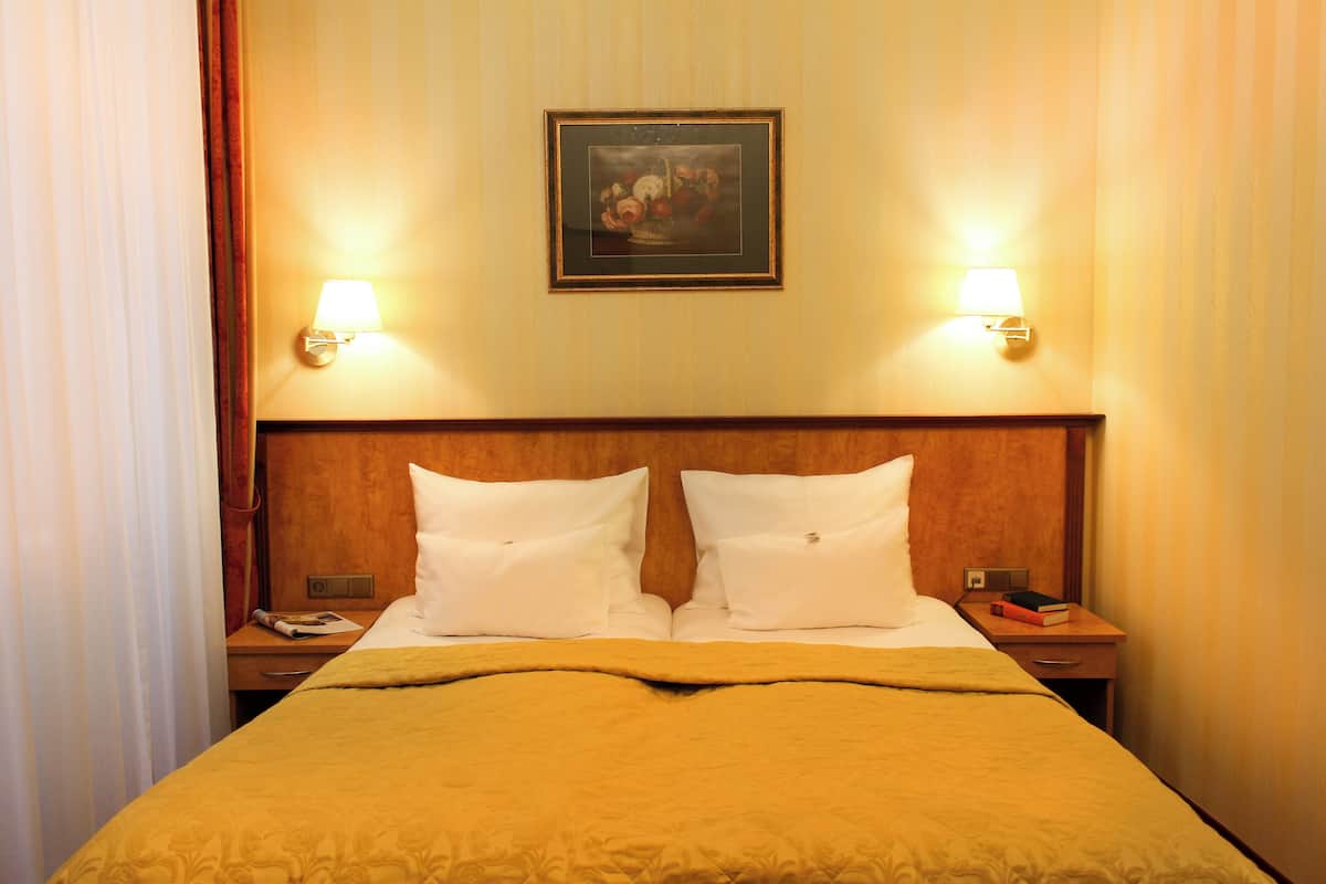 A hotel room with a bed, two bedside tables, a nightstand, a framed picture on the wall, and two wall-mounted lamps.
