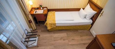 Una habitación de hotel con cama, mesita de noche, lámpara y un pequeño escritorio con silla.