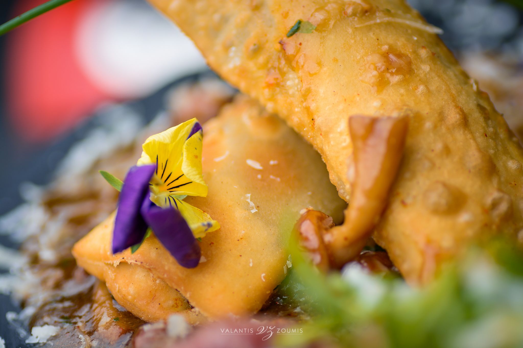 A close-up of a dish with a golden-brown crust, garnished with purple and yellow flowers.