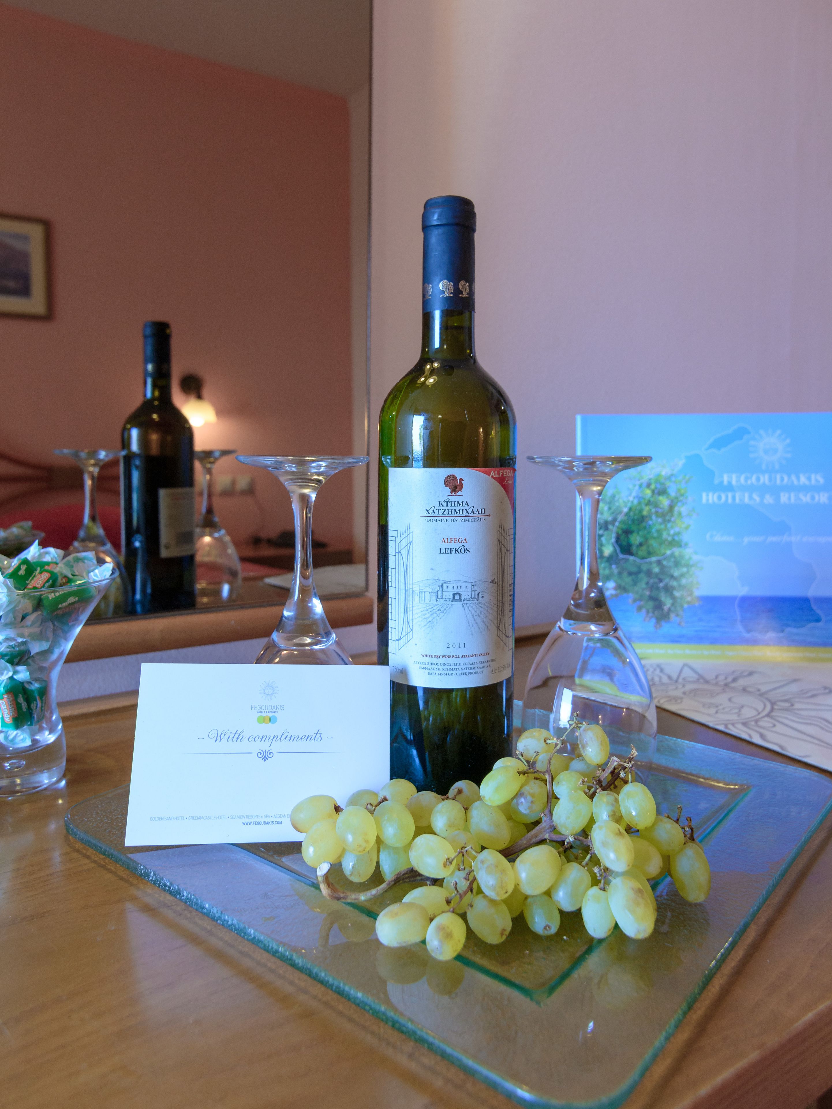 A table with a bottle of wine, glasses, a card, and a bunch of grapes.