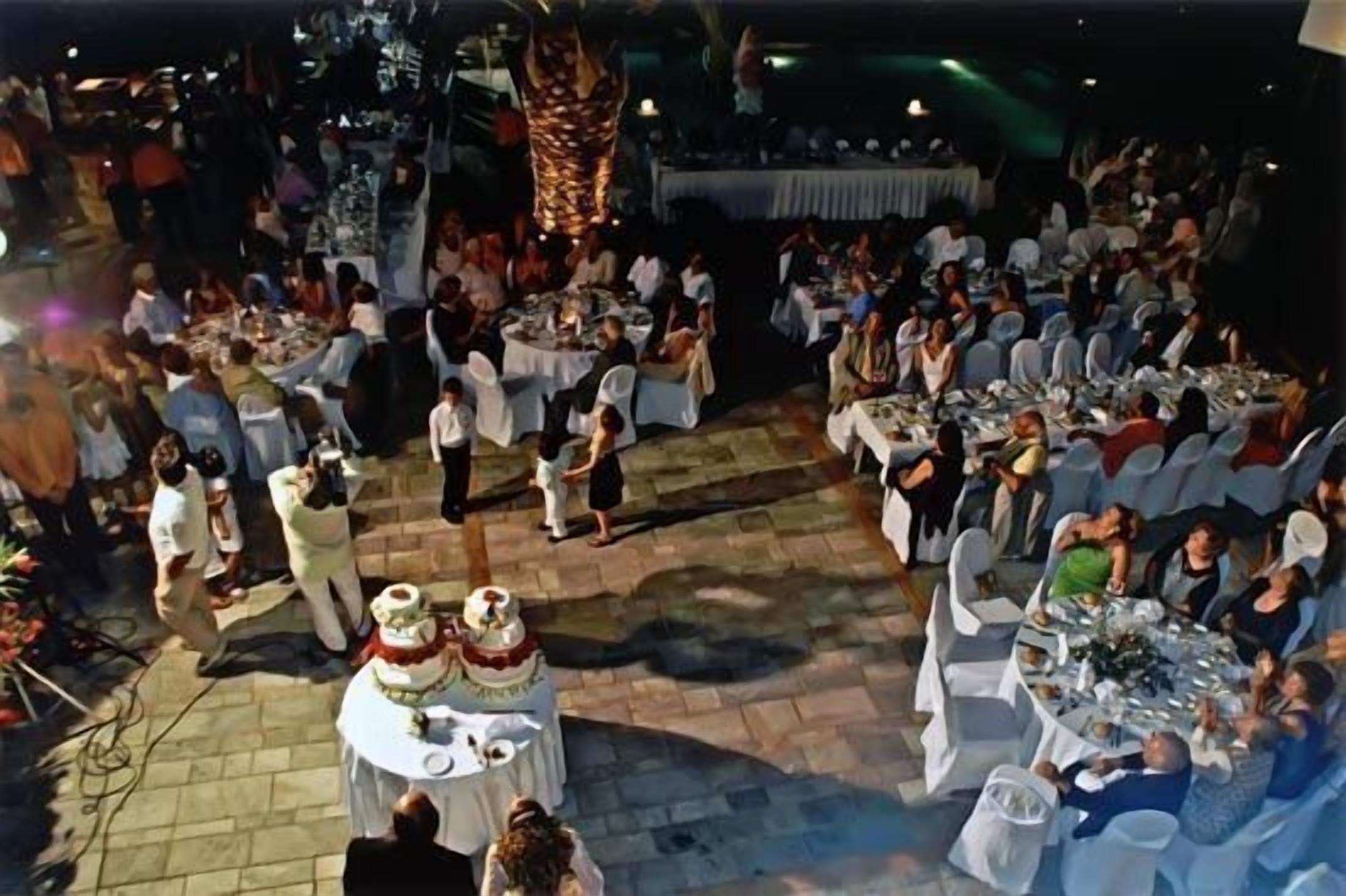 Evento al aire libre con mesas y sillas redondas, un escenario y una multitud de personas.