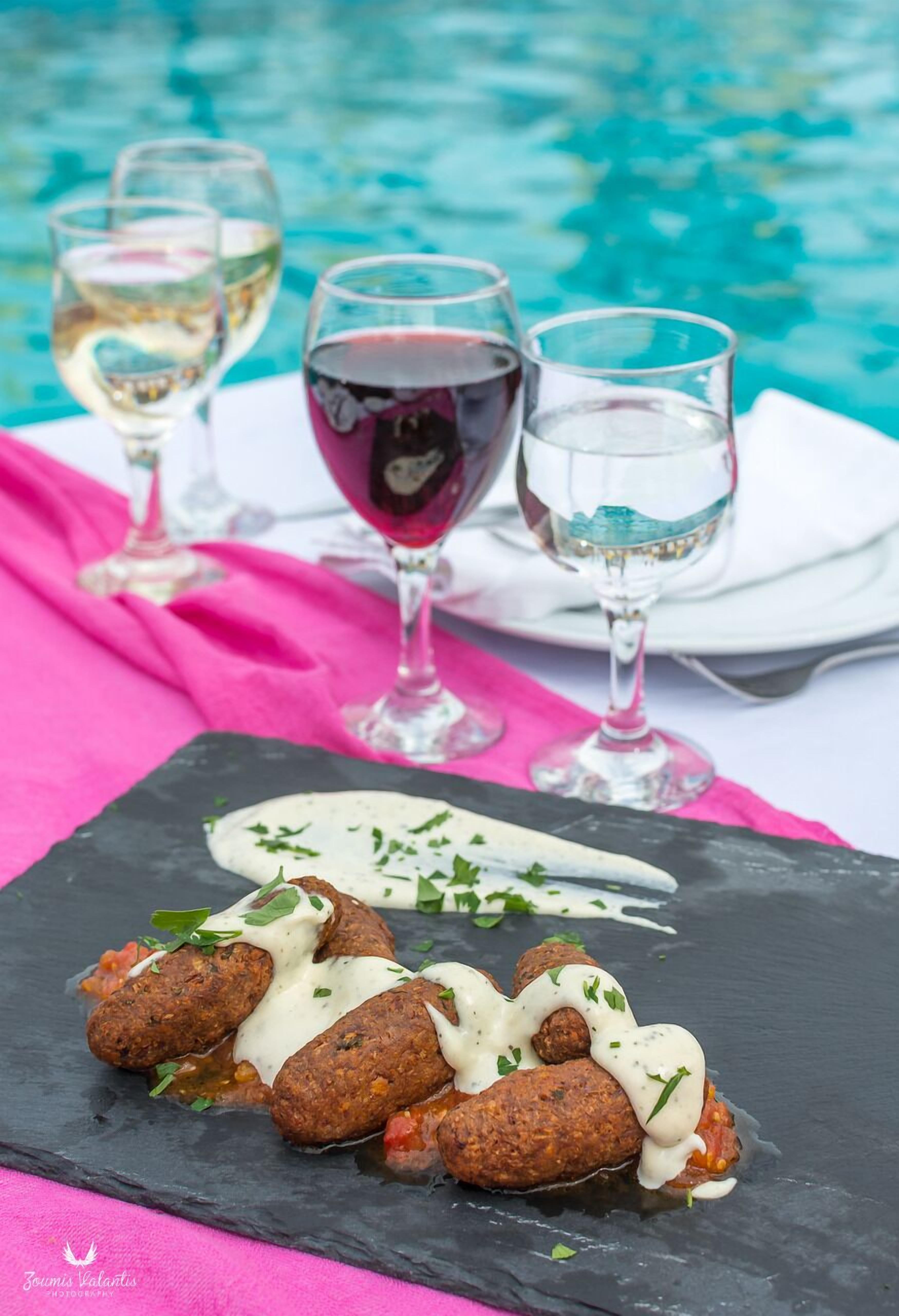 Un tavolo da pranzo con un piatto in ardesia nera pieno di cibo, accompagnato da tre bicchieri di vino, con vista sulla piscina.