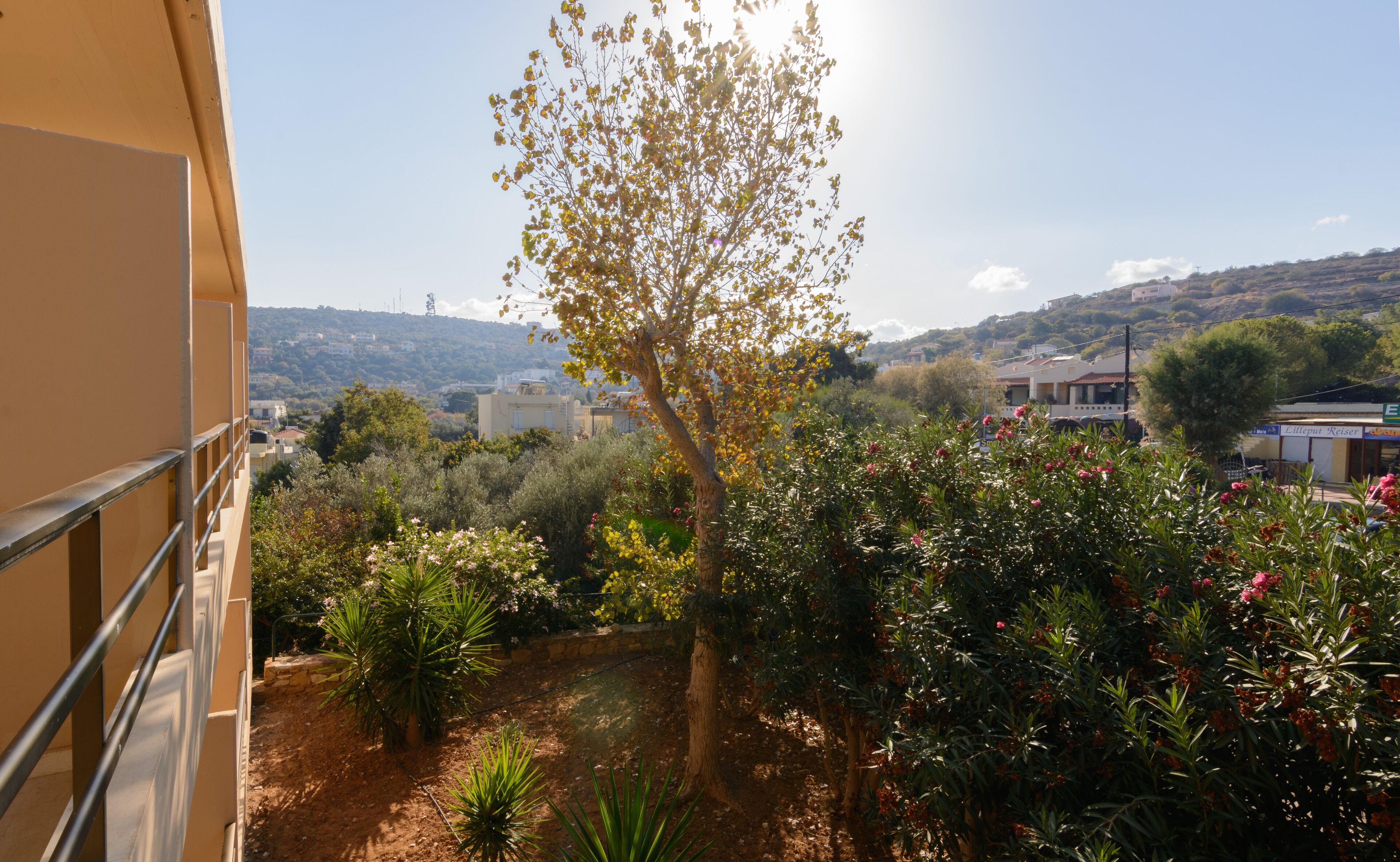 A balcony with a view of a garden, a tree, and a building in the background.