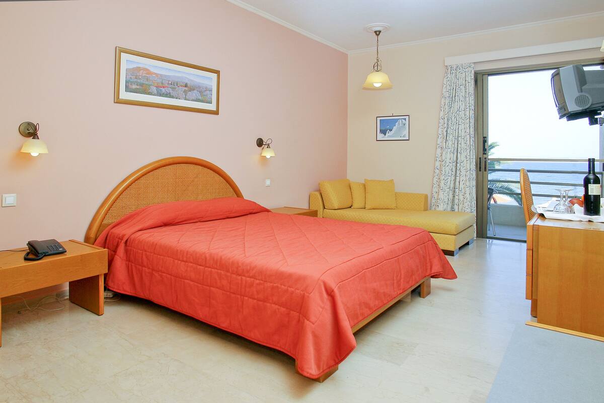 A hotel room with a bed, a sofa, a desk with a chair, and a balcony with a view.