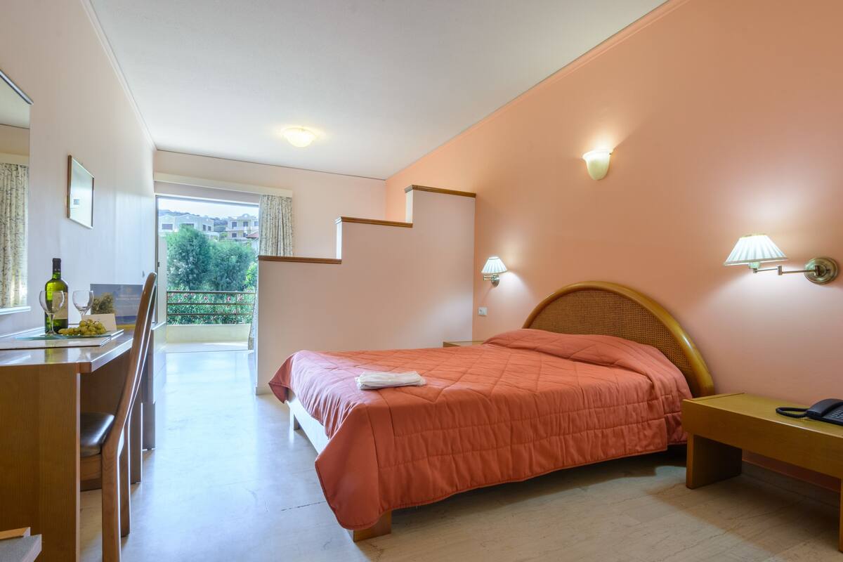 A bedroom with a bed, bedside table, lamp, and a view of the outdoors.