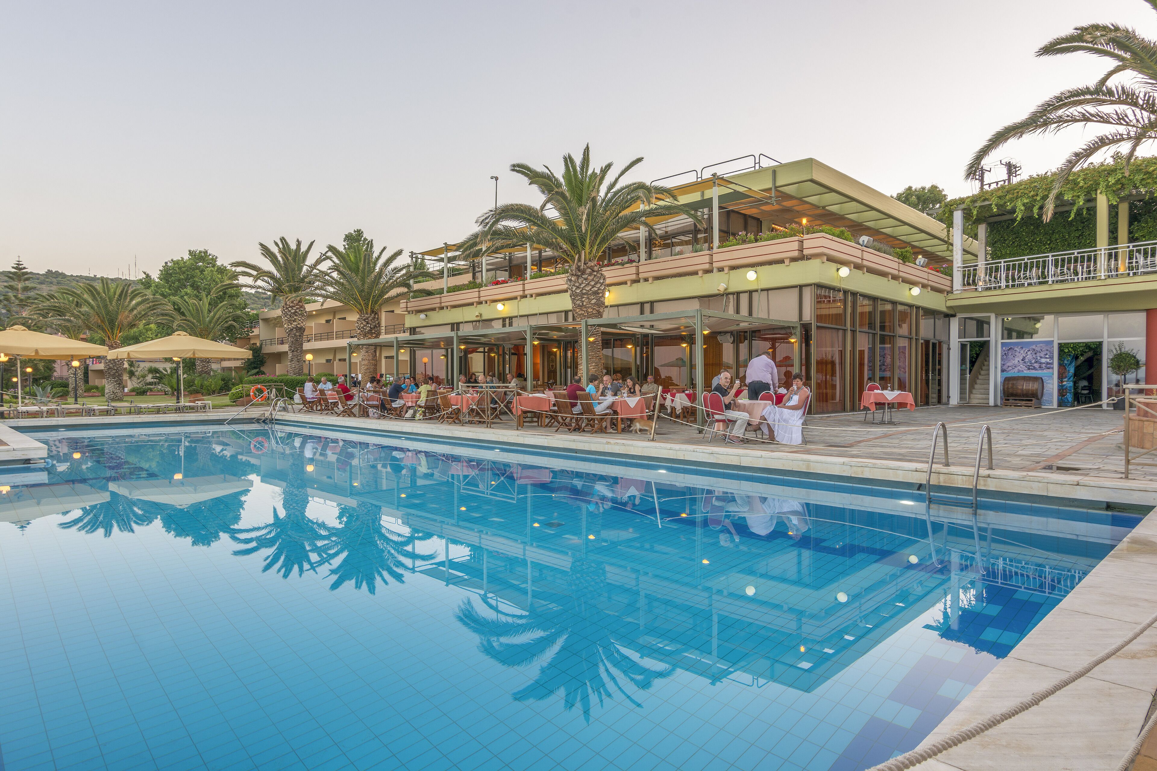 A hotel with a swimming pool, outdoor seating, and palm trees.