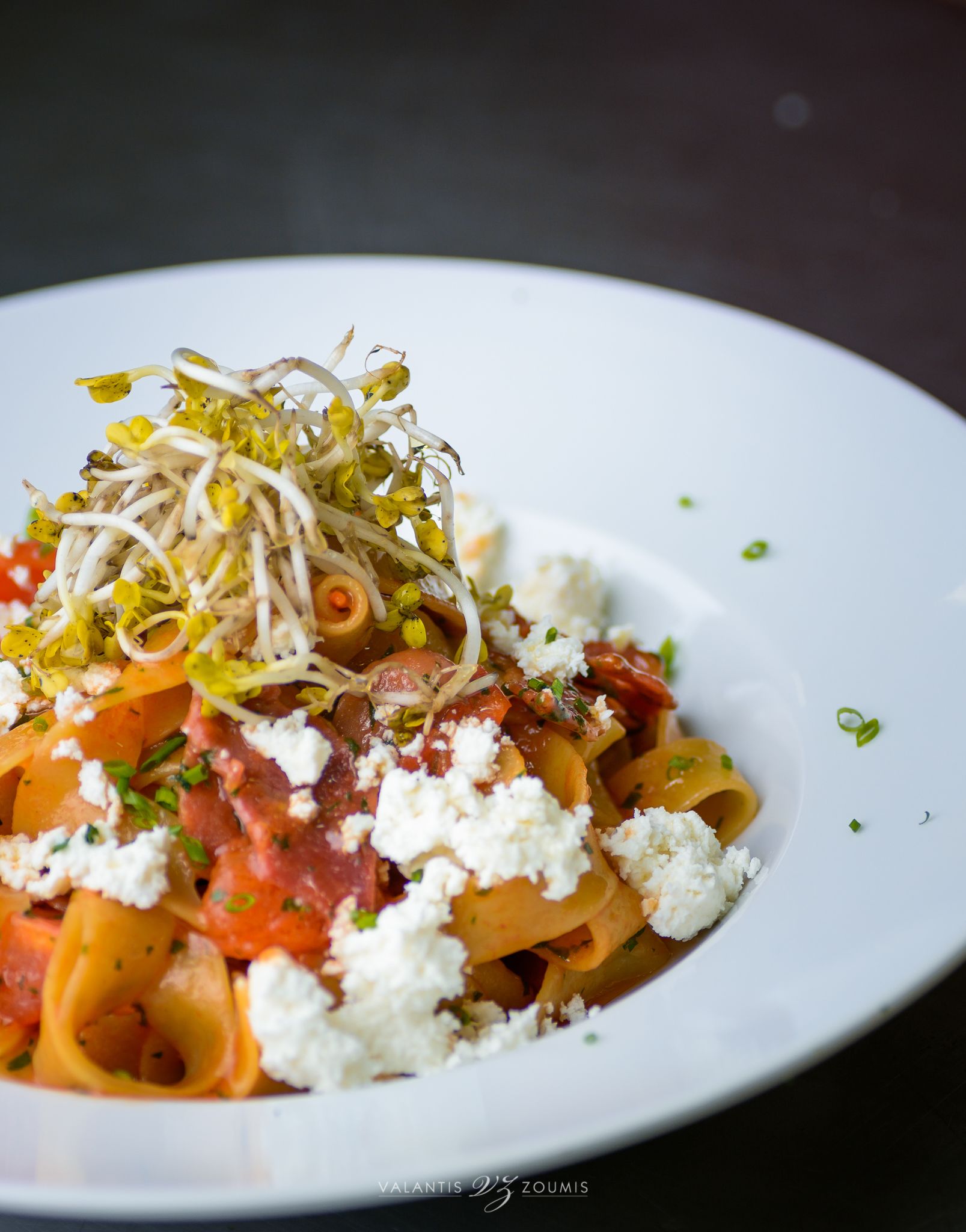 A plate of pasta with a creamy sauce, topped with green onions and a white creamy substance.