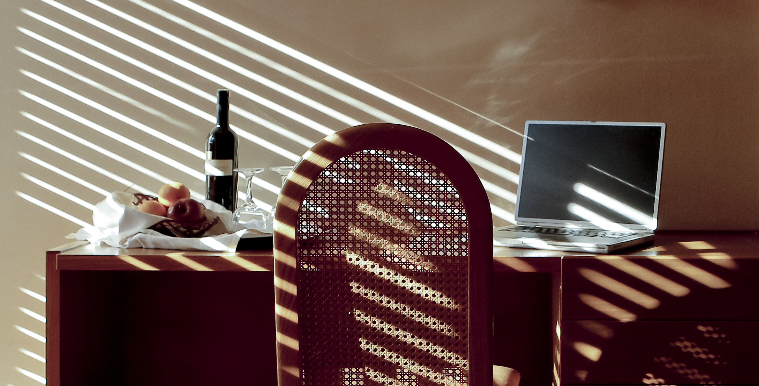 Una computadora portátil sobre un escritorio de madera, con una botella y vasos, y un objeto con diseño en primer plano.