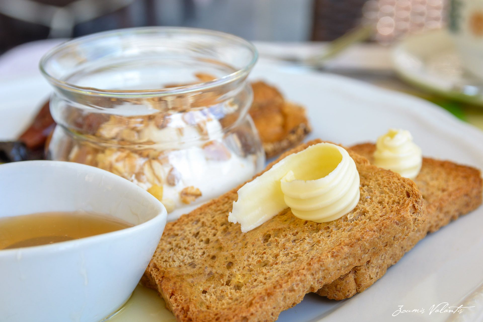 A plate with a slice of toast topped with butter, a small bowl of jam, and a cup of tea.