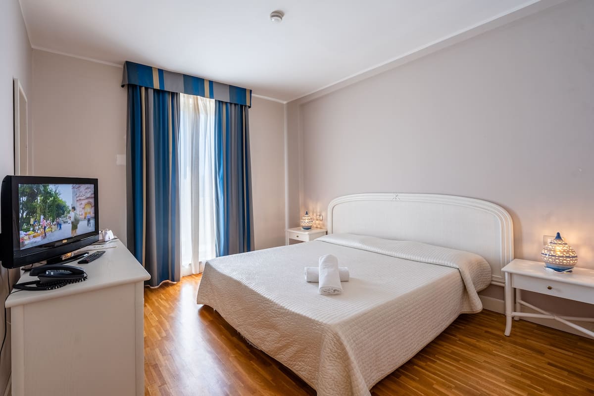 A hotel room with a bed, a TV, a desk, and a nightstand with a lamp.