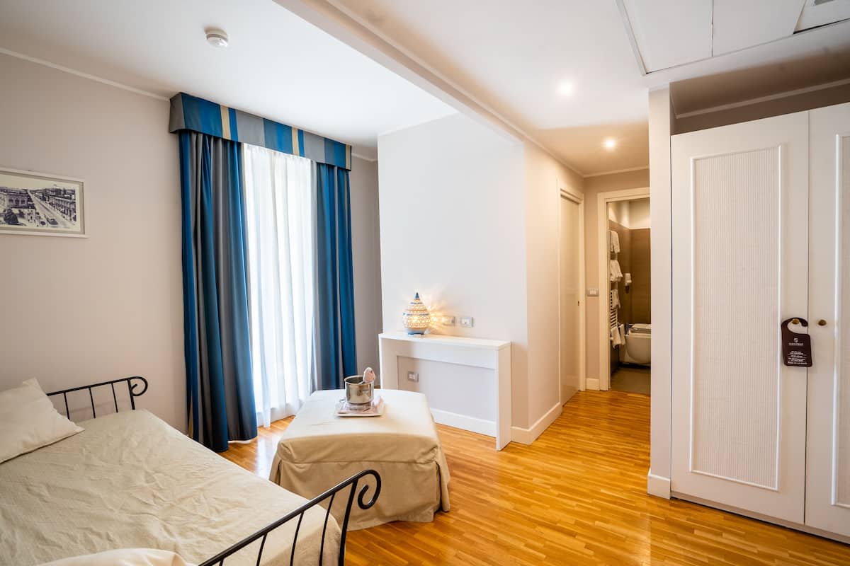 A hotel room with a bed, a bedside table with a lamp, a desk, and a wardrobe.