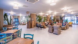 A spacious indoor area with multiple seating arrangements, including tables and chairs, and a variety of plants. - Capo Peloro Resort - Adults Only (Messina)