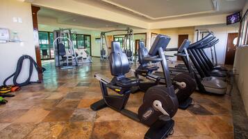 Une salle de sport équipée de divers appareils d’exercice, notamment des tapis de course et des appareils de musculation, et dont le sol est carrelé.