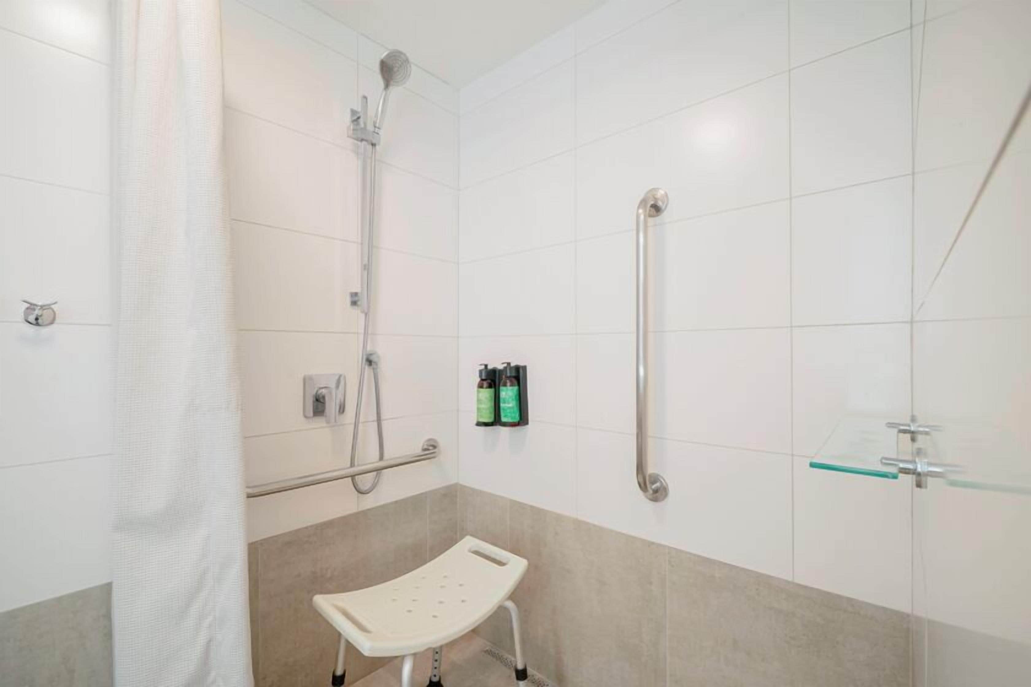 A shower area with a handheld showerhead, a glass shelf, and a white step for accessibility.
