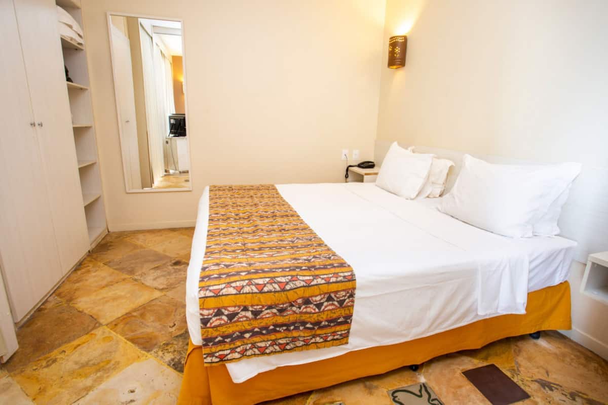 Una habitación de hotel con cama, mesita de noche, espejo y armario.