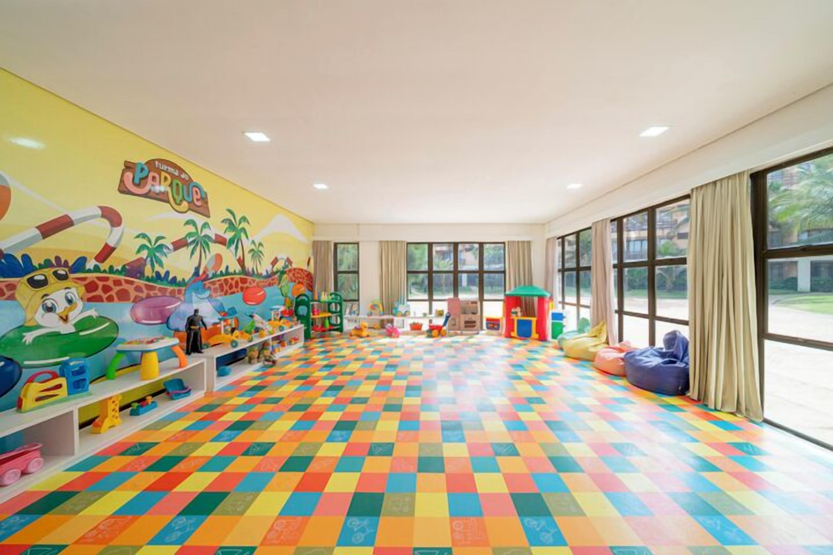 A brightly colored playroom with a checkered floor, colorful toys, and a mural on the wall.