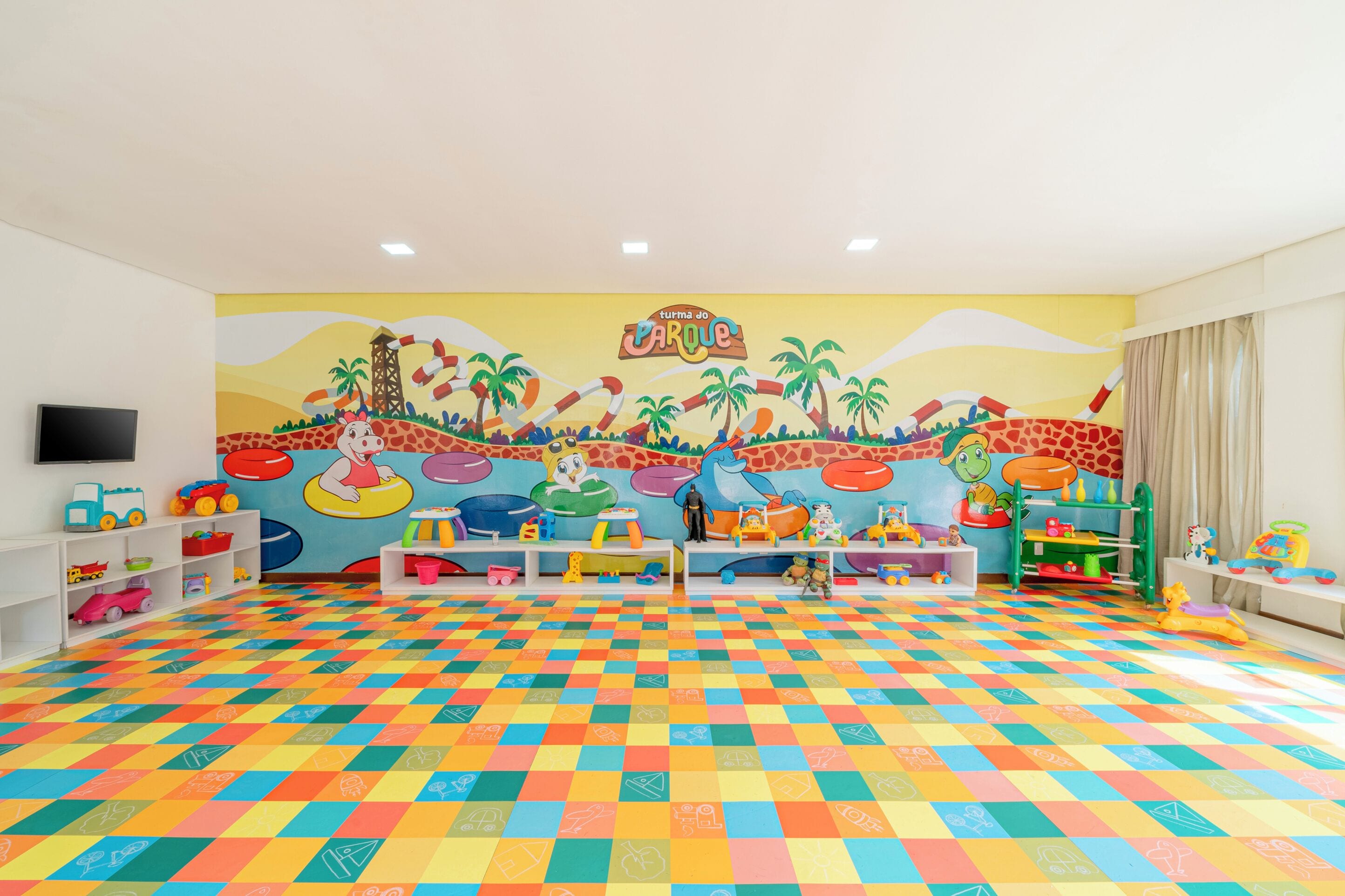 A brightly colored playroom with a checkered floor, shelves with toys, and a mural depicting a park scene.