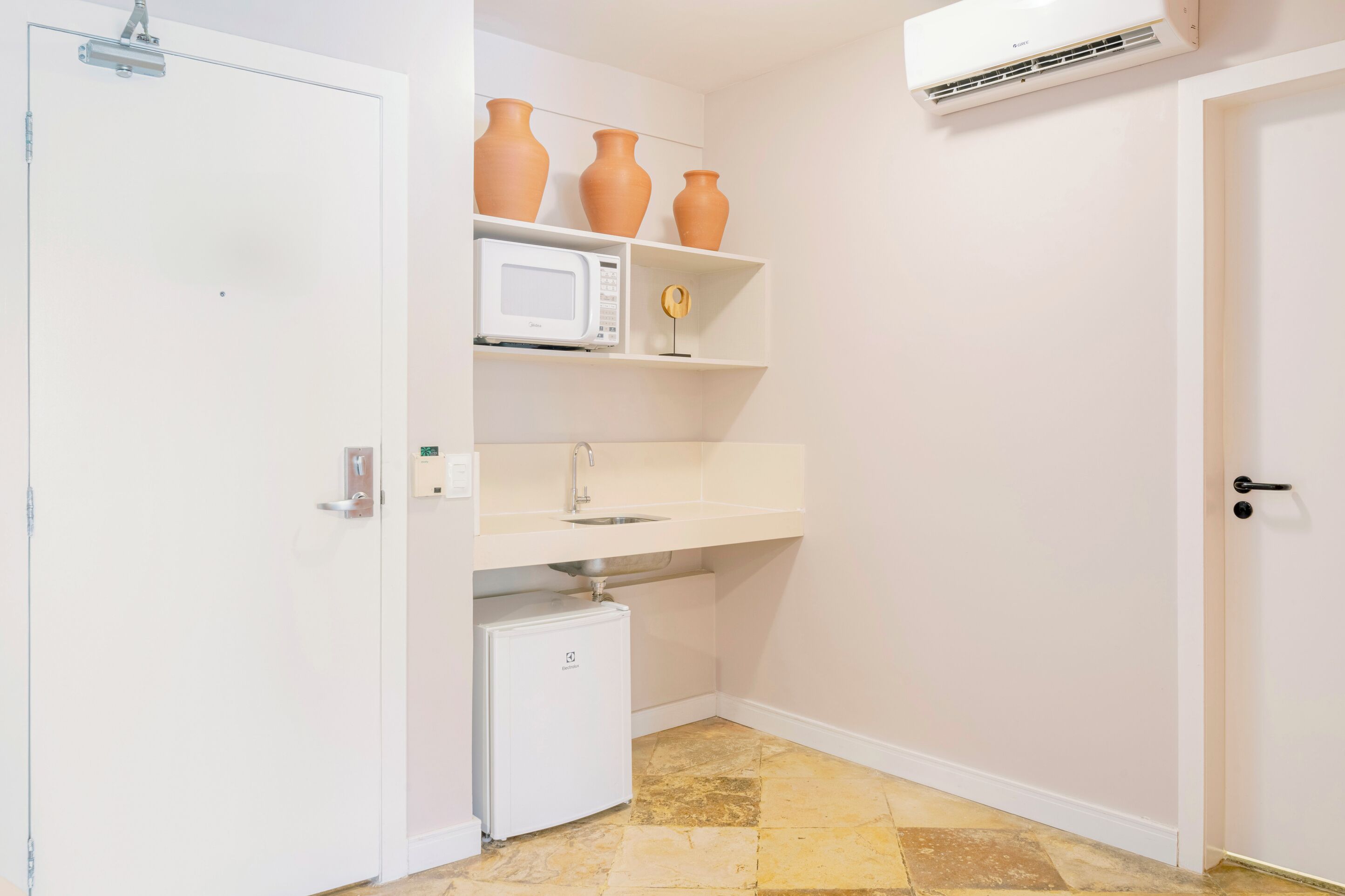 A compact kitchen with white cabinets, a microwave, a small refrigerator, and three ceramic vases on a shelf.