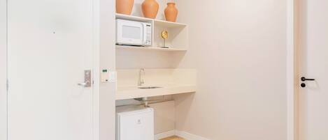 A compact kitchen with white cabinets, a microwave, a small refrigerator, and three ceramic vases on a shelf.