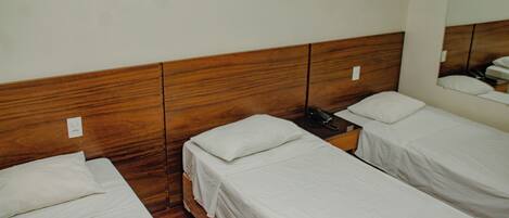 A hotel room with two single beds, wooden headboards, white bedding, and a bedside telephone.