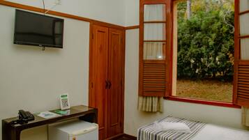 Una habitación con una cama, un escritorio con computadora, un teléfono y una ventana con vista a zonas verdes.