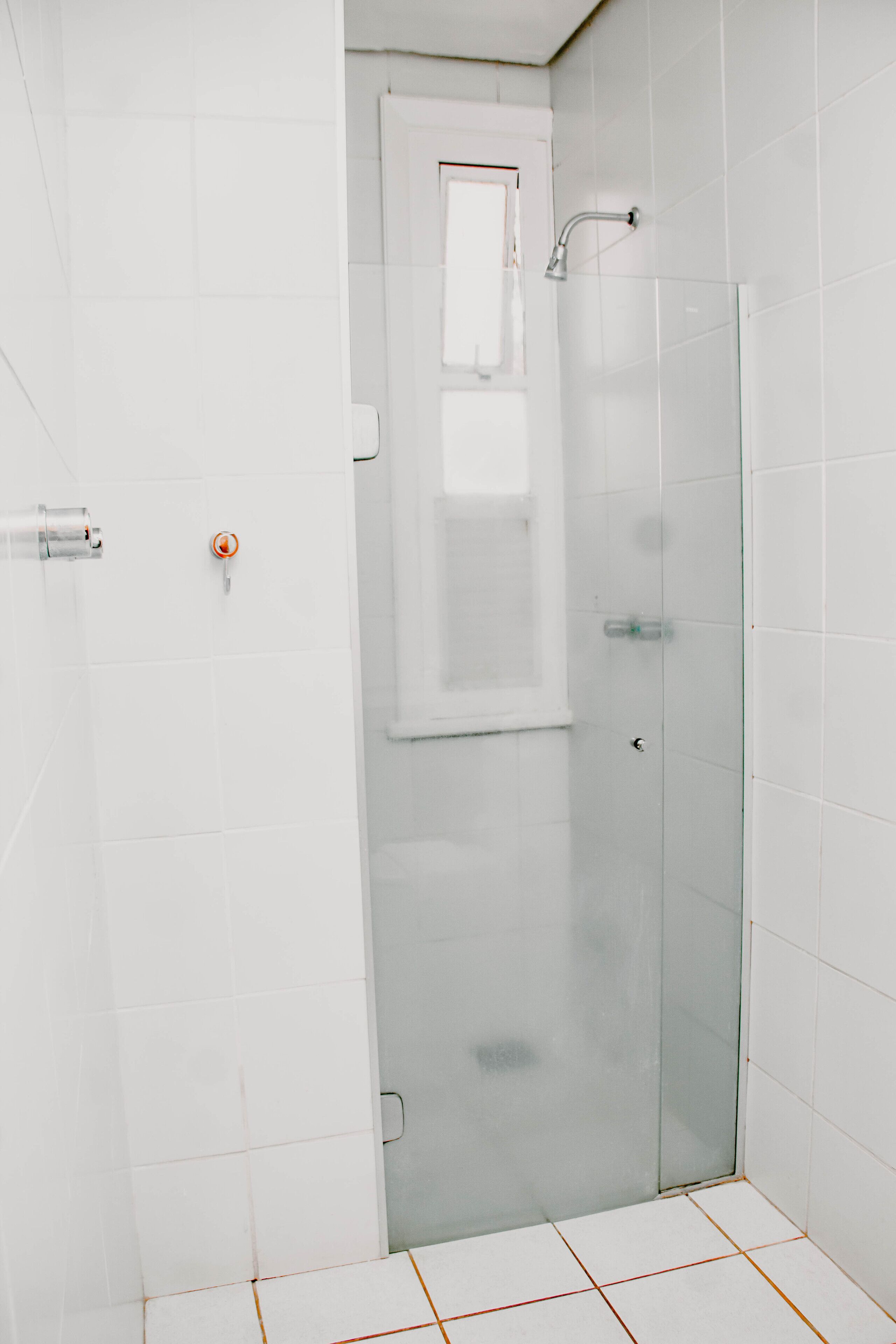 A bathroom with white tiled walls, a glass shower enclosure, and a door with a handle.
