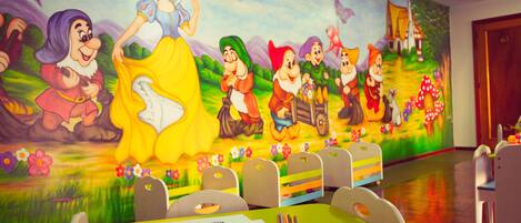 Une chambre d’enfant ornée d’une fresque représentant des personnages de Disney, une table verte avec du matériel de dessin et de peinture, et un plancher en bois.