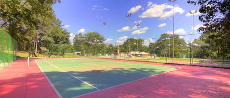 An outdoor tennis court with a green and red surface, surrounded by trees and a fence.