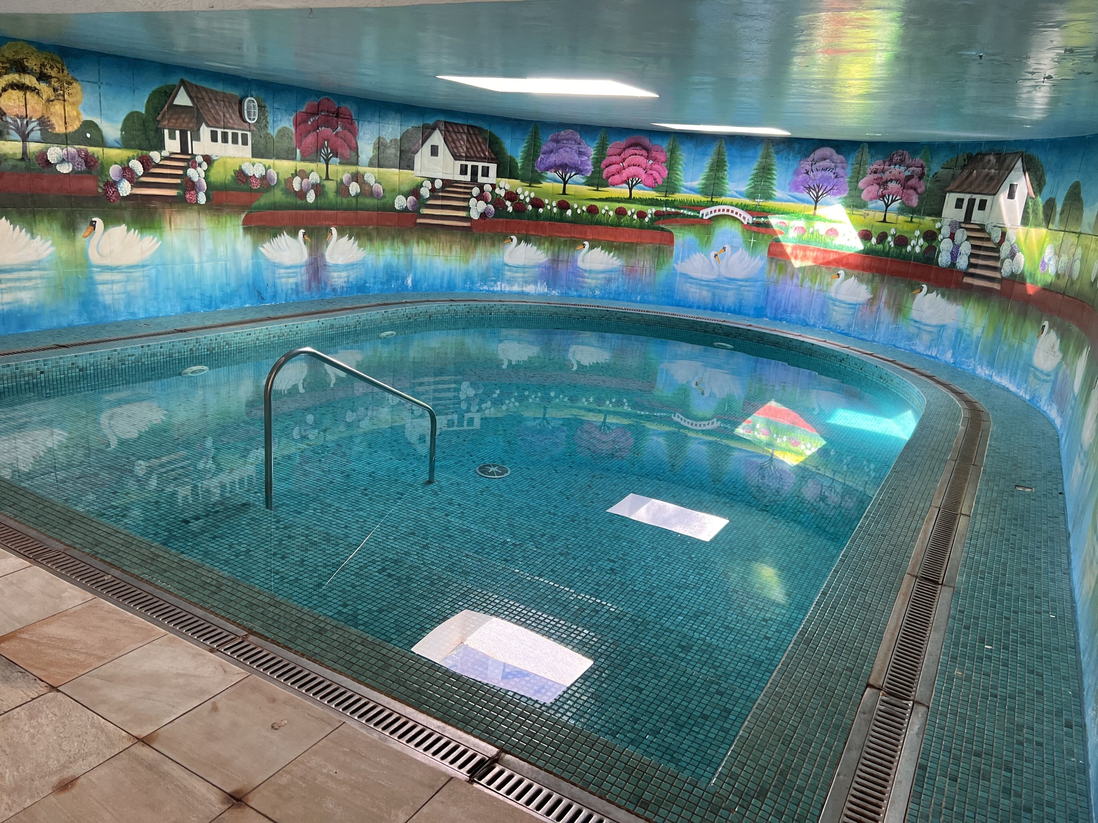 Piscina interna com um mural nas paredes retratando uma paisagem e casas.