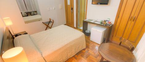 A hotel room with a bed, a desk, a chair, a TV, and a lamp.