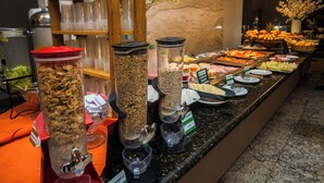 Un bufé con diversos alimentos y recipientes, como cereales, yogur y frutas.