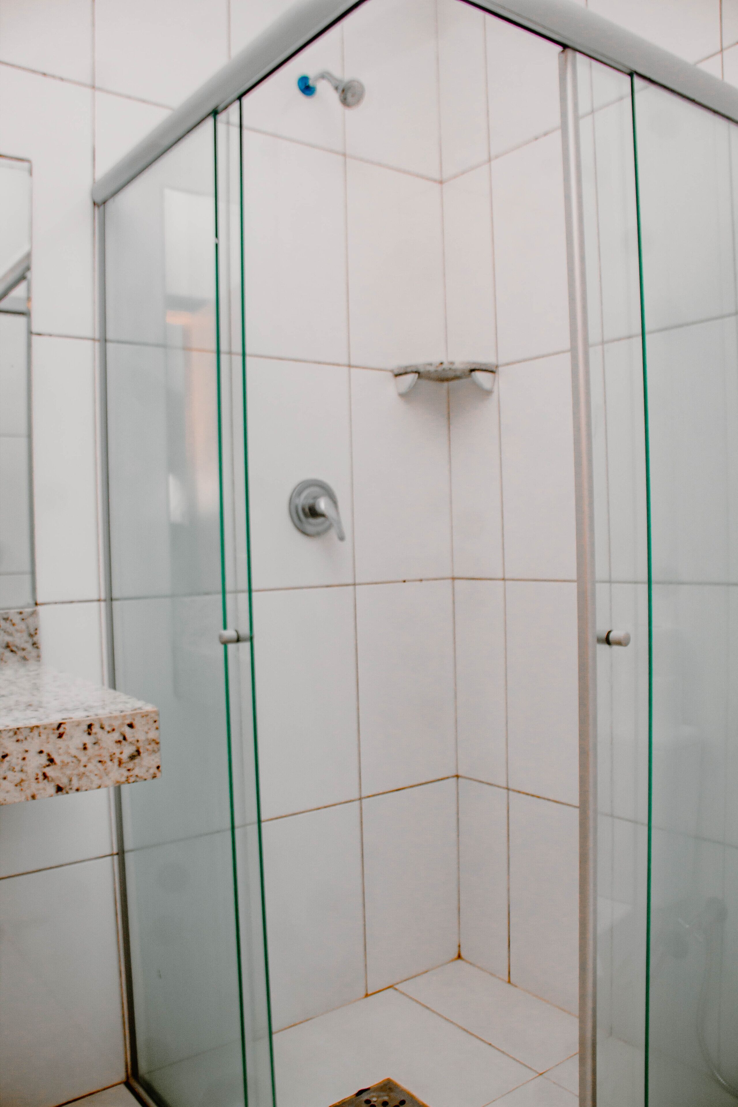 Un vestidor de ducha con paredes de vidrio, azulejos blancos, un cabezal de ducha de metal y un pomo de cristal.