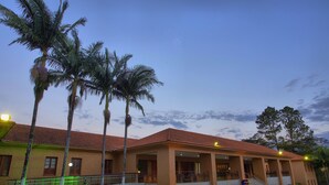 Un hotel con techo de tejas rojas, palmeras y un área de entrada pavimentada.