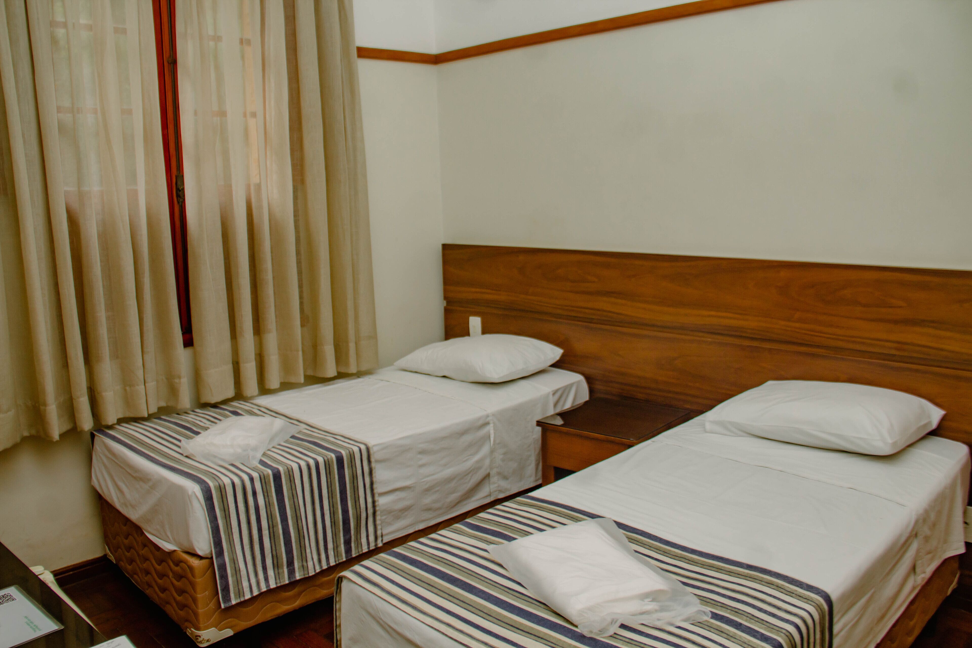 Une chambre d’hôtel avec deux lits simples, des têtes de lit en bois et une table de chevet en bois placée entre les deux lits.