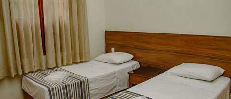 Une chambre d’hôtel avec deux lits simples, des têtes de lit en bois et une table de chevet en bois placée entre les deux lits.