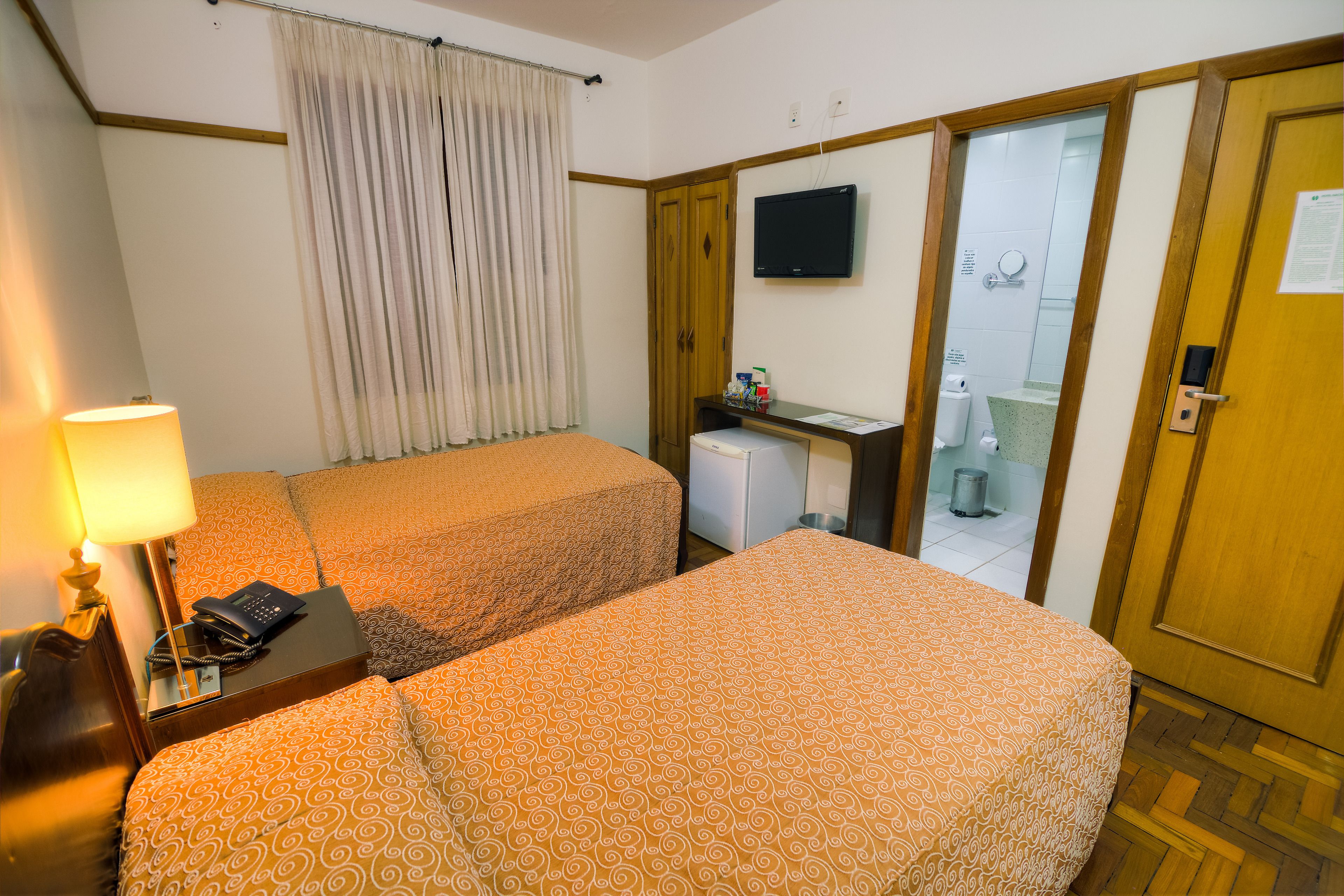 Een hotelkamer met twee bedden, een bureau met een computer, een televisie, en een badkamer die door een open deur zichtbaar is.