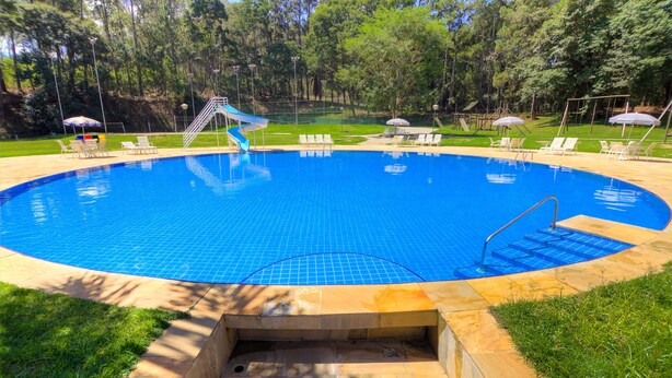 Una piscina circular con un tobogán, rodeada de césped y árboles.
