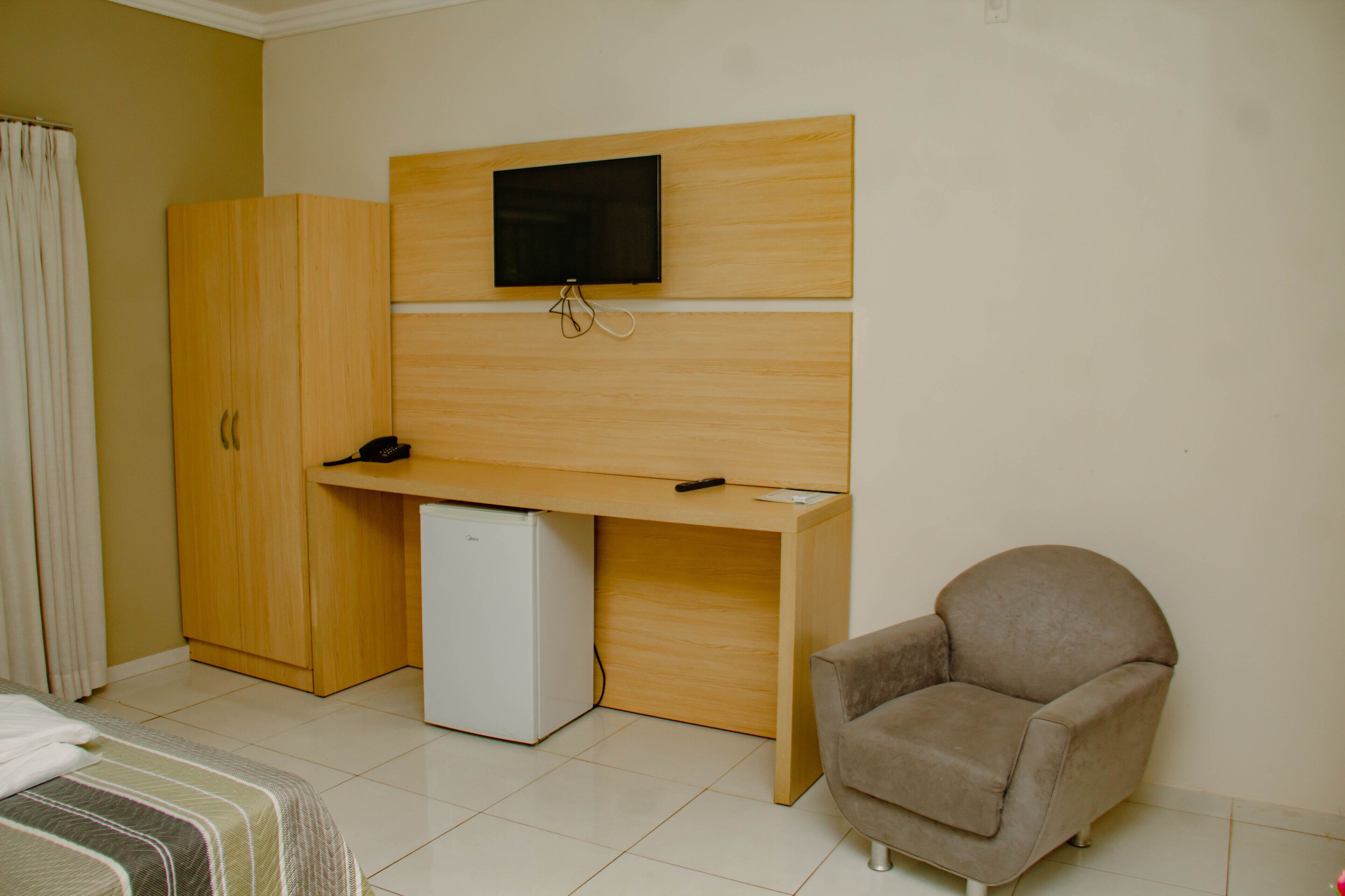 A bedroom with a bed, a desk with a television, a chair, and a wardrobe.