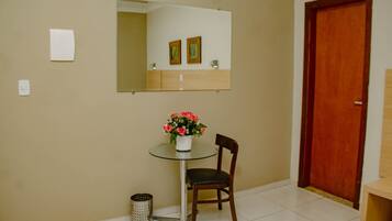 Una habitación pequeña con una mesa redonda, una silla, un espejo, una puerta de madera y un cubo de basura.