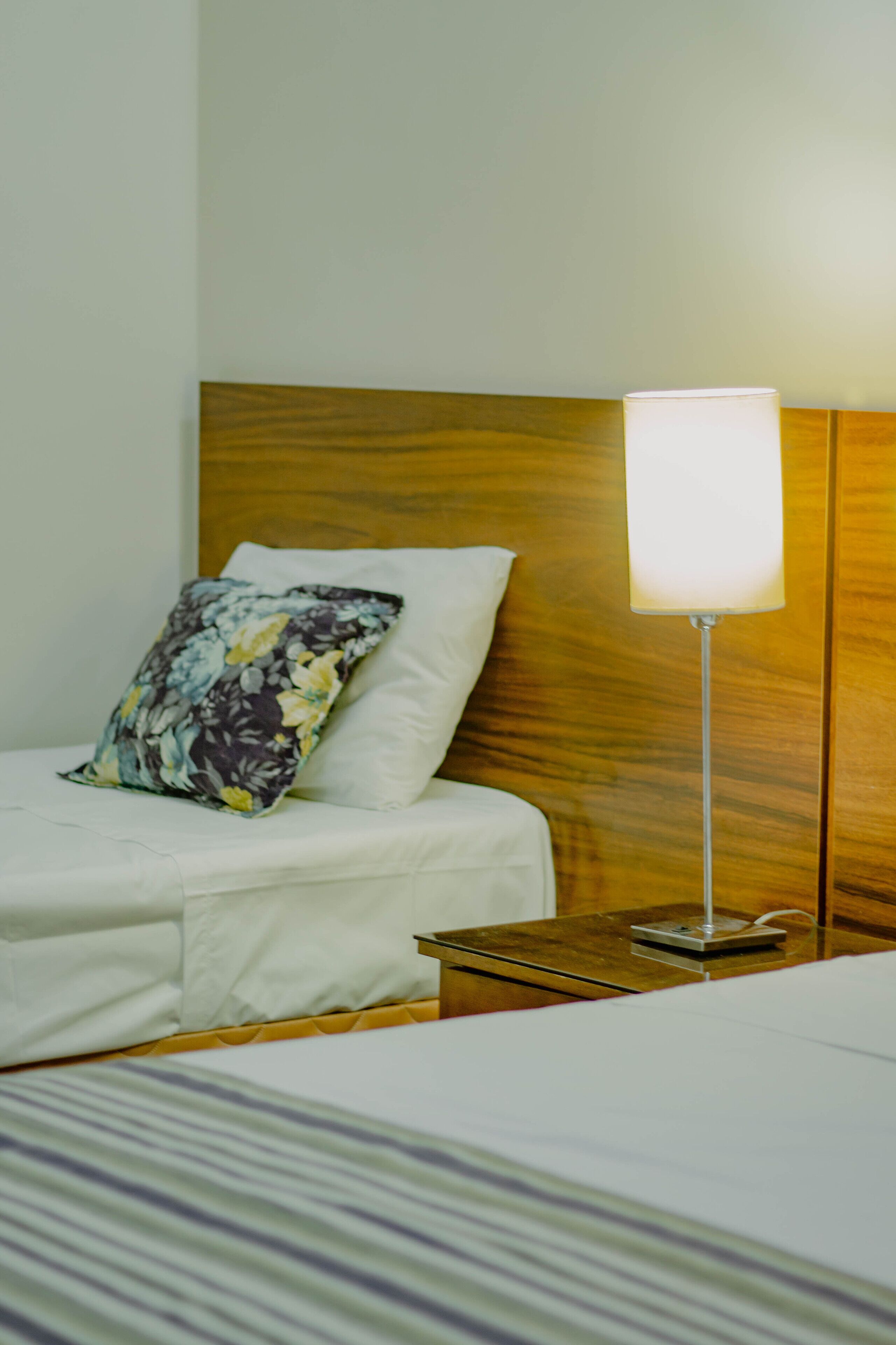 Un lit bien fait, agrémenté d’un coussin à motifs floraux, d’une table de chevet et d’une lampe.